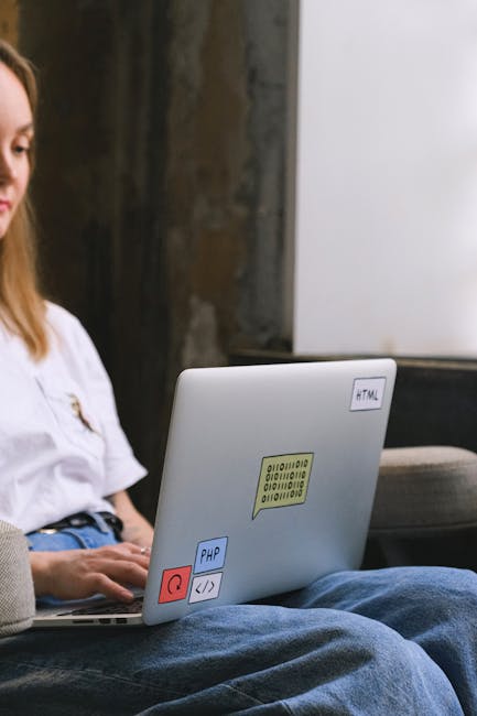 The image shows a young woman seated indoors in a modern, minimalistic setting with a concrete wall and a white door or panel in the background. She has long, light brown hair and is wearing a casual